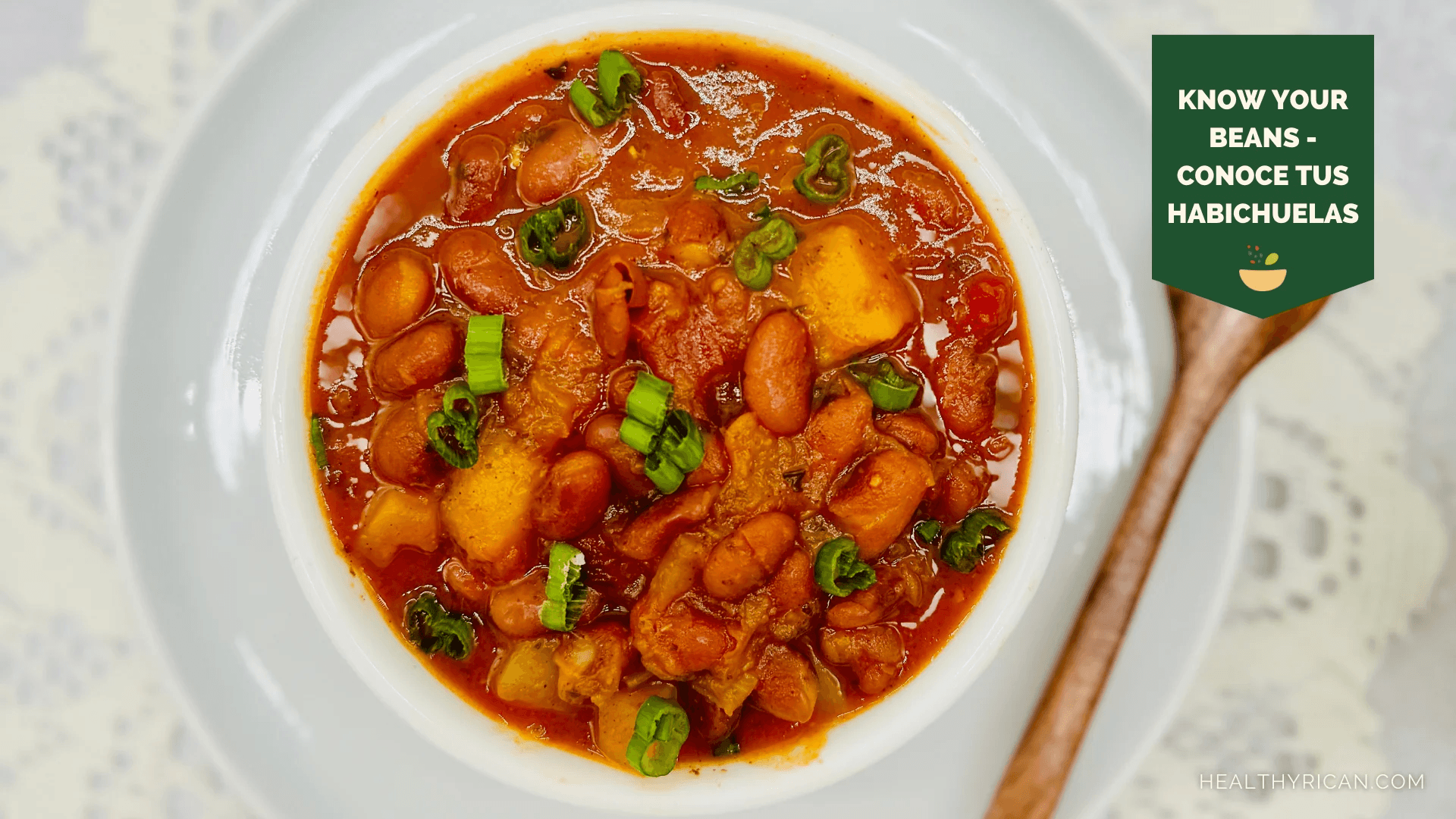 Puerto Rican stewed beans in tomato broth with potatoes and scallions, served in a white bowl.