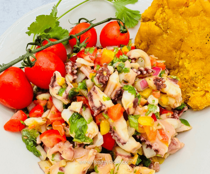 Puerto Rican ensalada de mariscos with octopus, peppers, cilantro, cherry tomatoes, and mofongo on a white plate.