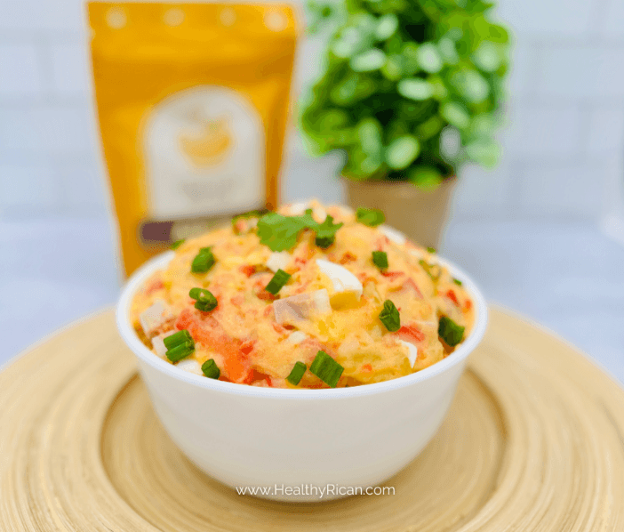 Puerto Rican potato salad with egg, peppers, and scallions in a white bowl, garnished with cilantro.