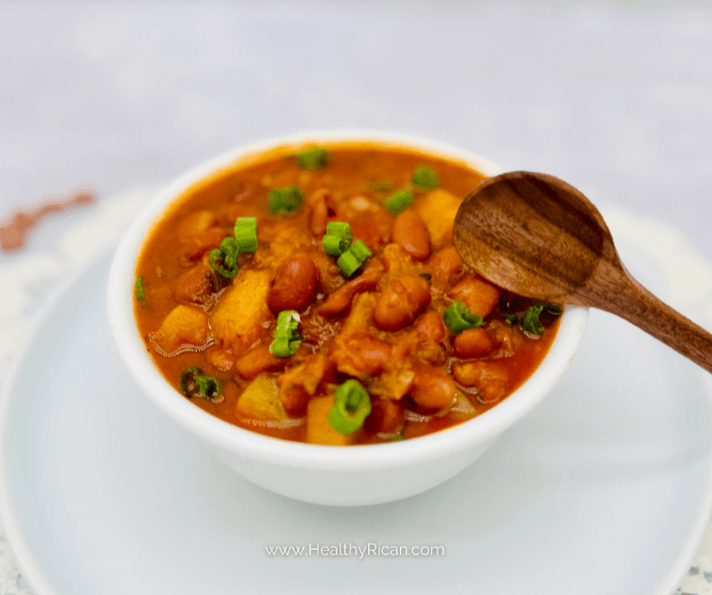 Puerto Rican stewed beans with potatoes and scallions in a white bowl, served with a wooden spoon.
