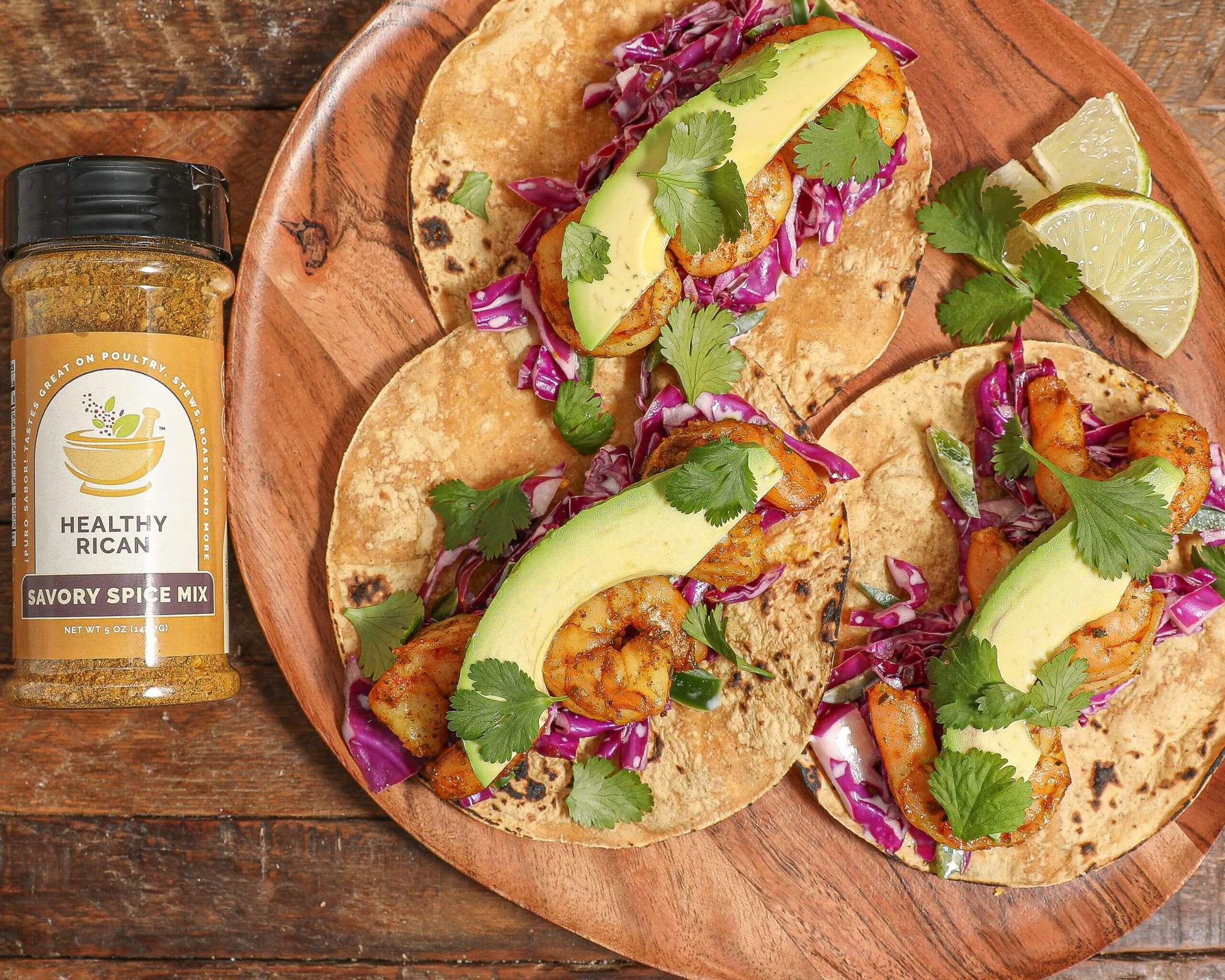Shrimp tacos topped with avocado, purple cabbage slaw, and cilantro beside Healthy Rican Savory Spice Mix.