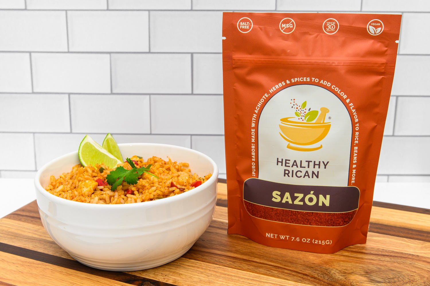 Healthy Rican Sazón seasoning pouch beside a bowl of Puerto Rican rice with lime wedges and cilantro.